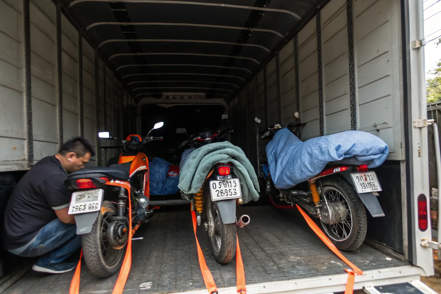 Several motorcycles secured with soft straps and blankets inside a covered truck
